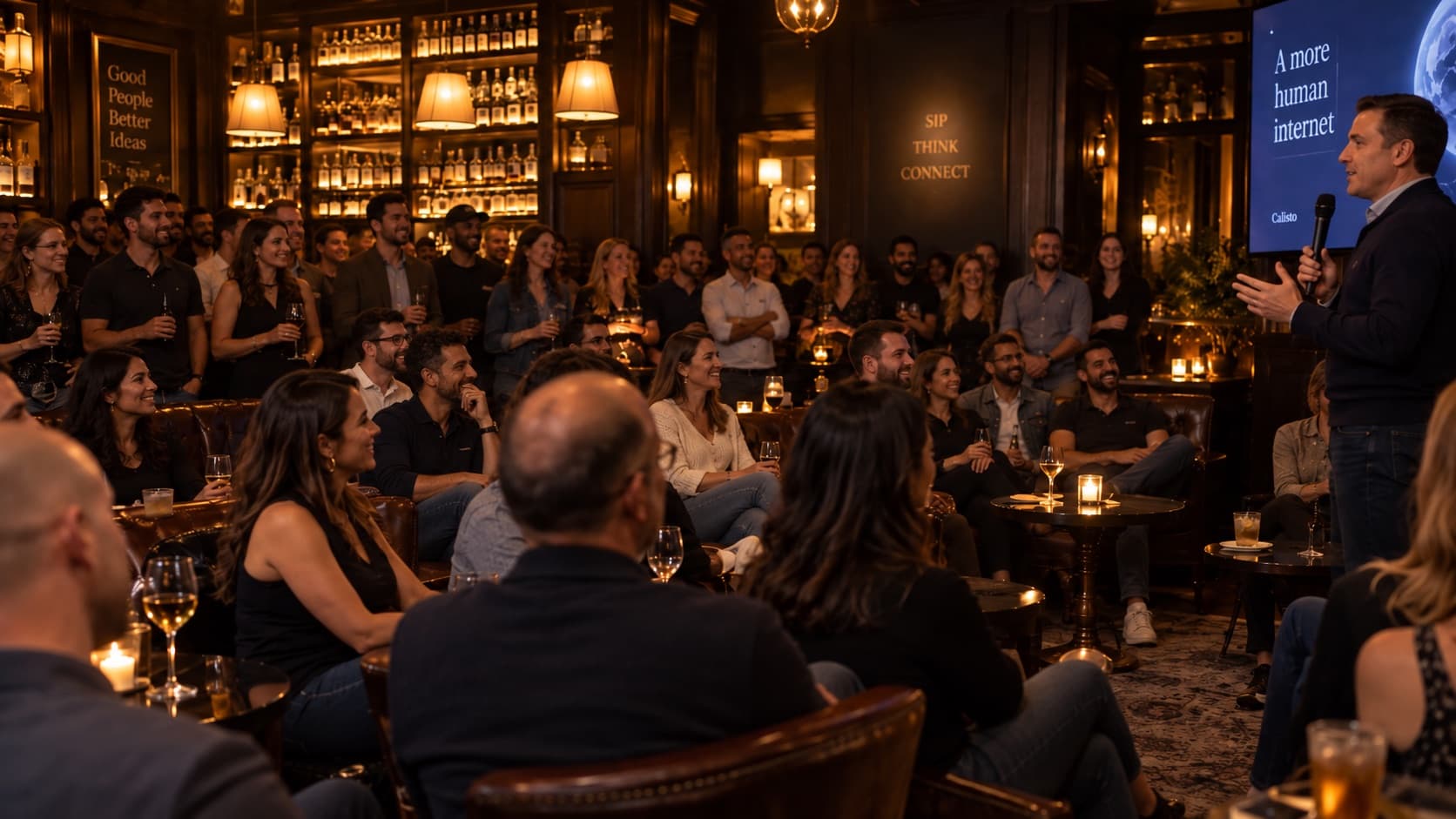A crowd listening to a speaker in a warmly lit New York bar.